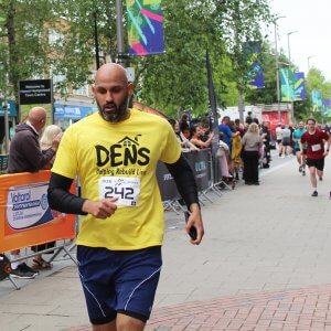 A man running, wearing a DENS t-shirt